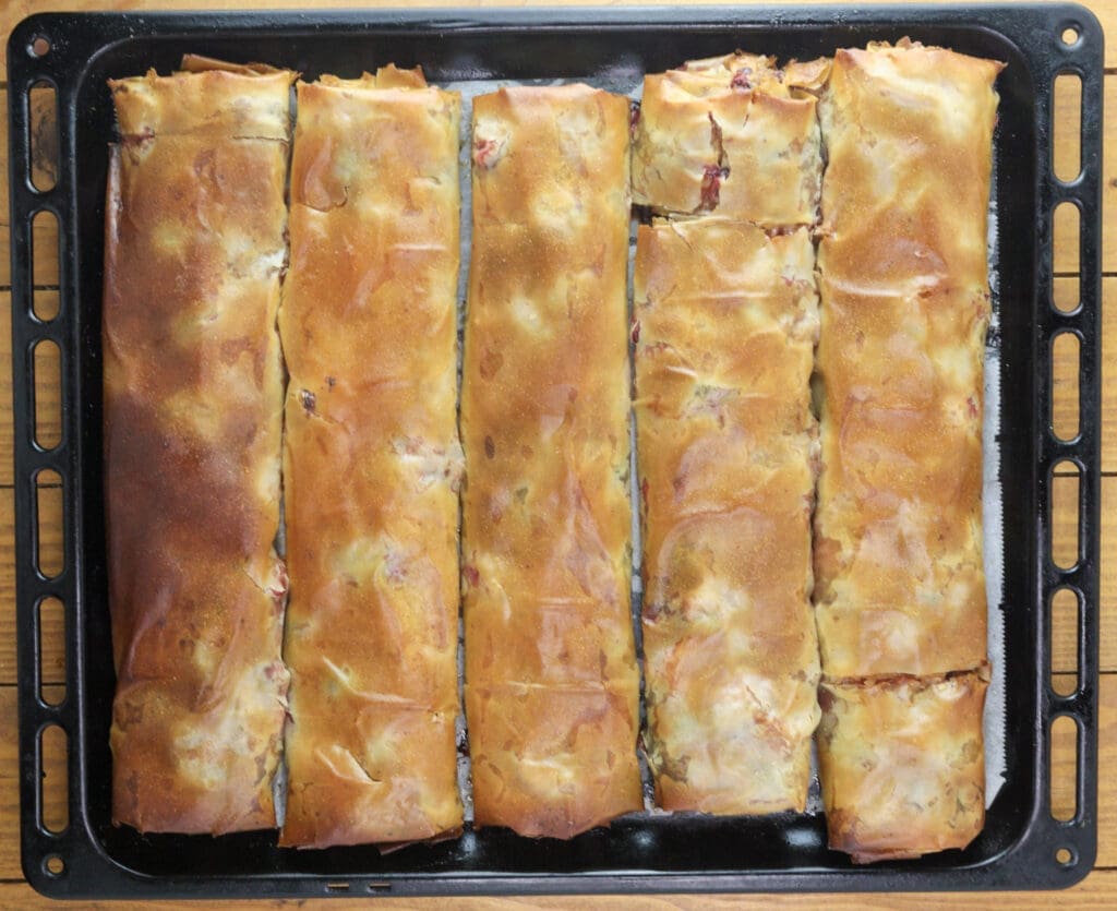 Five freshly baked strudel rolls coming out of the oven.